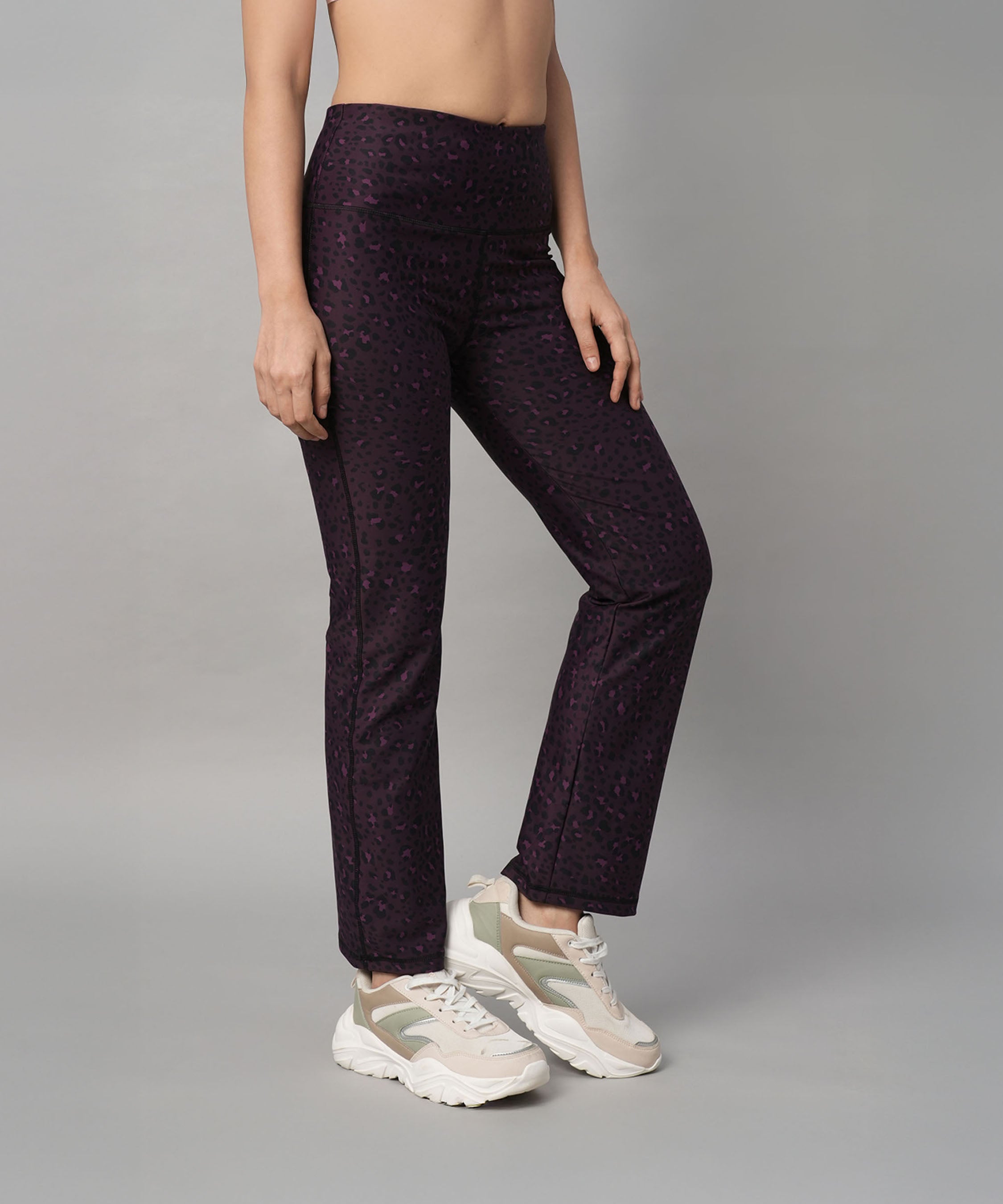 Person wearing Pink Animal Print Wide Legged Leggings and white sneakers, standing against a plain gray background.