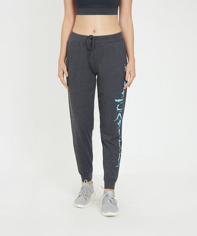 A woman in TUNA LONDON Joggers - Ashtanga Series Grey, paired with a black crop top and gray sneakers, stands confidently against a white background—a chic and comfy look for stylish women.