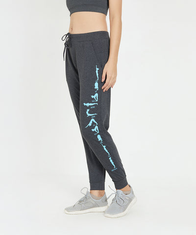A woman in TUNA LONDON Joggers - Ashtanga Series Grey with blue text on the leg, a grey crop top, and grey sneakers, standing sideways.