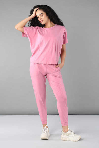 Model showcases the Baby Pink Co-Ord Set, featuring a soft cotton lycra t-shirt and elastic waistband trousers paired with white sneakers, for a stylish and breathable look against a plain gray backdrop.