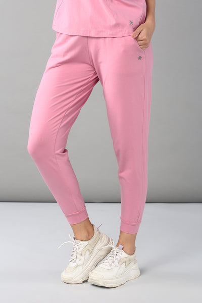 Someone stands against a plain gray background wearing the Baby Pink Co-Ord Set featuring joggers with an elastic waistband, paired with white sneakers to highlight a comfortable and breathable look.