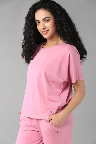 Woman with long curly hair wearing the Baby Pink Co-Ord Set—pink cotton lycra t-shirt and matching elastic waist trousers—smiling at the camera in this comfortable, breathable outfit.