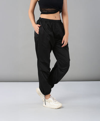 Woman wearing Black Parachute Pants with an adjustable waist and white sneakers poses against a plain gray background.