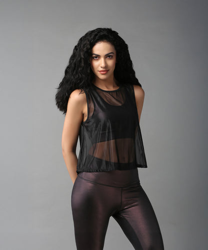 A woman with long curly hair models the Black Sheer Top and shiny leggings, posing against a plain gray background.