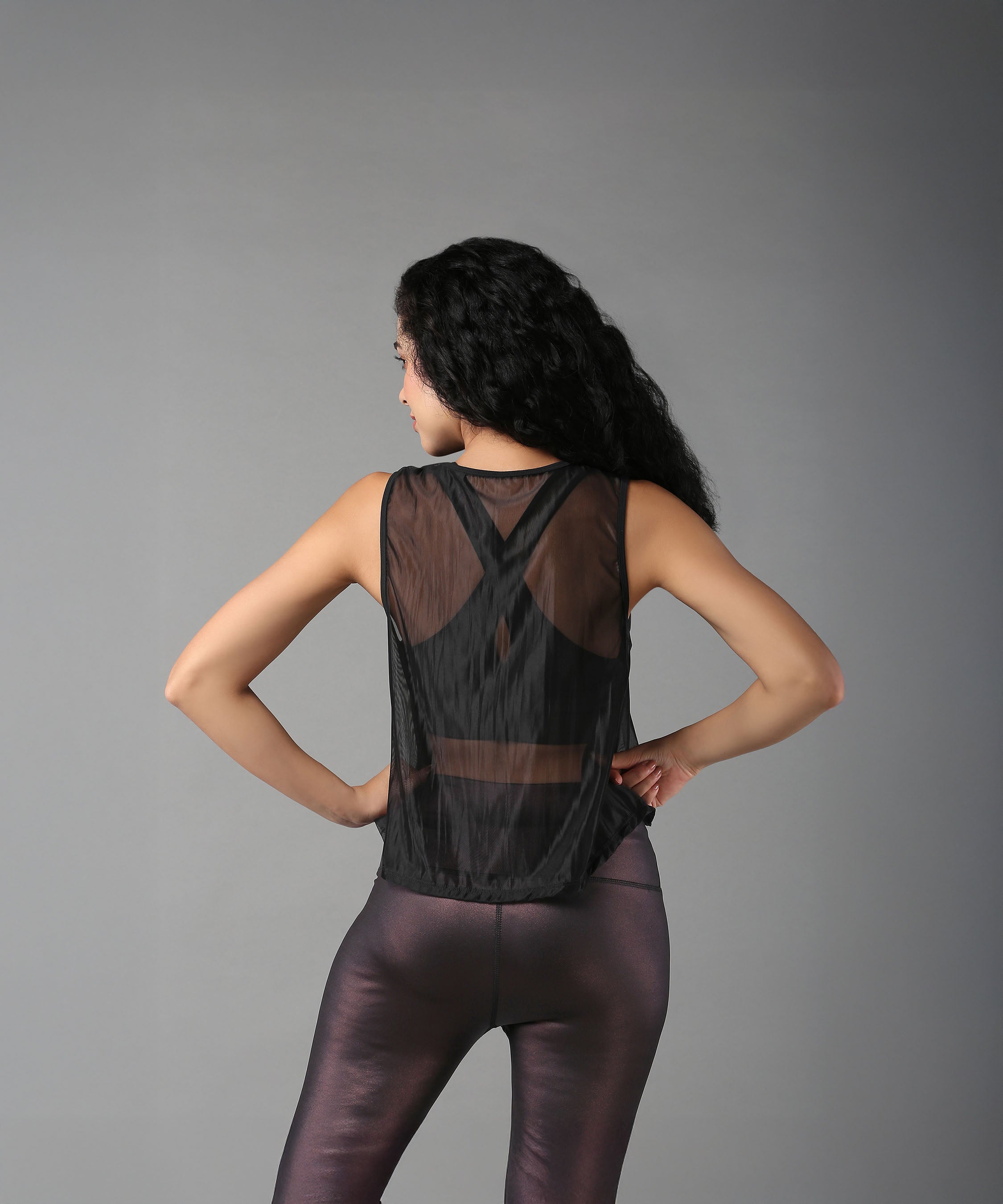 Woman models the Black Sheer Top, standing with hands on hips and facing away.