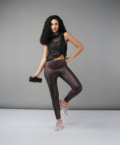 Confident woman poses against a gray background wearing headphones, a Black Sheer Top, shiny workout clothes, and holding a water bottle.