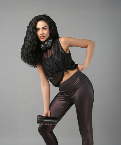 A woman wearing the Black Sheer Top poses with headphones around her neck and a water bottle in hand, set against a gray background.