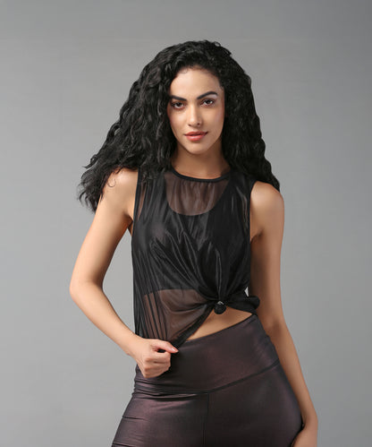 Woman with long curly hair poses in a Black Sheer Top and shiny leggings against a gray background.