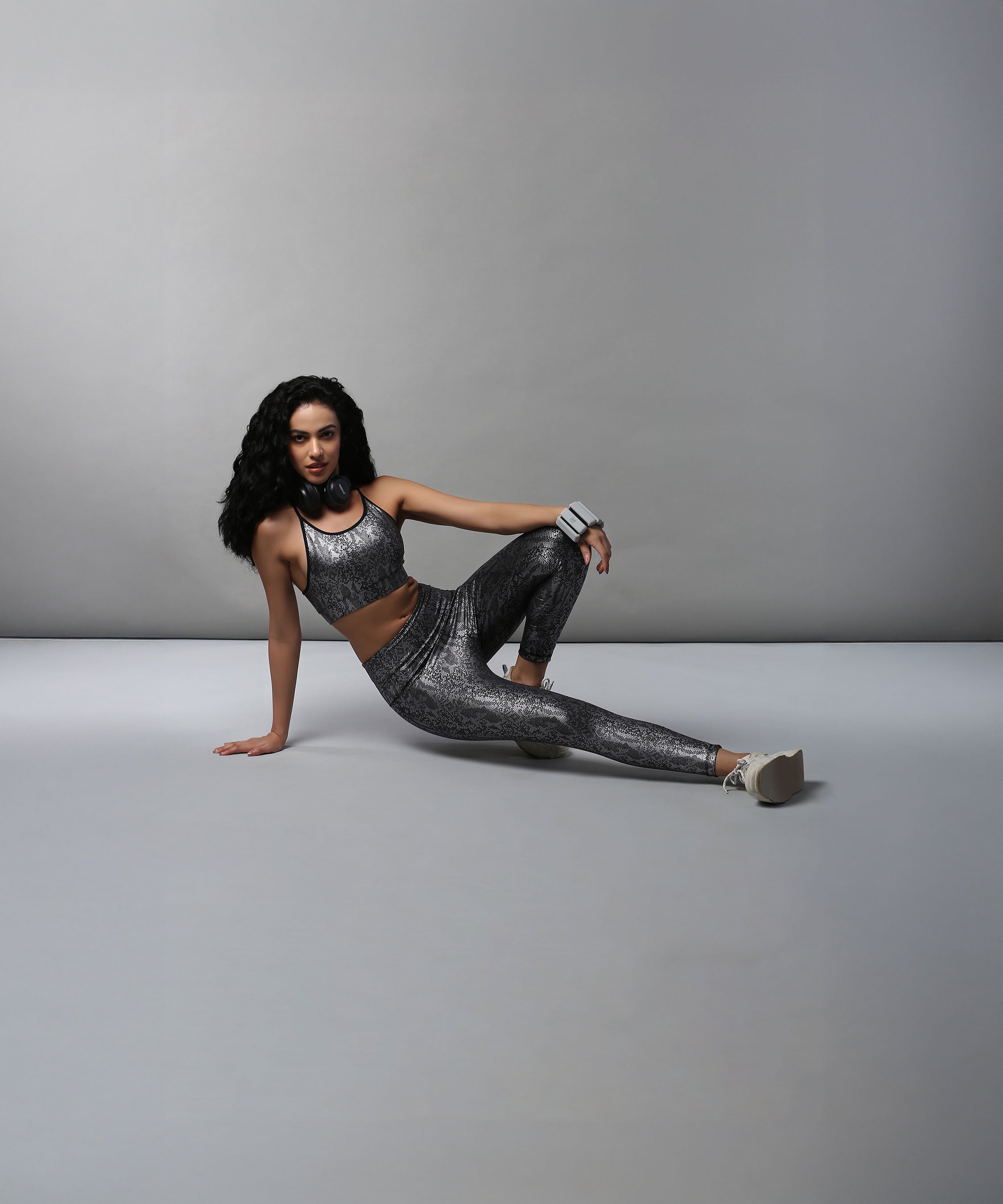 A woman models the Black Silver Shimmer Leggings, sitting on the floor in gray athletic wear against a plain gray background.