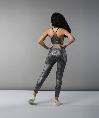 Woman with long curly hair stands facing away, wearing the Black Silver Shimmer Print Sports Bra and high waisted Leggings set.