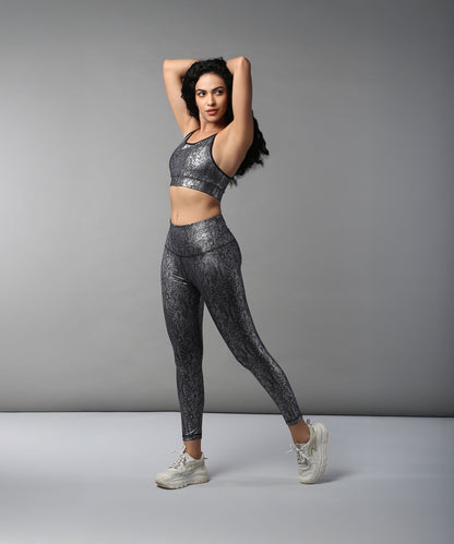 Woman in Black Silver Shimmer Print Sports Bra and Leggings, made from moisture-wicking fabric, poses against a plain gray background.
