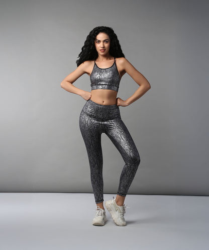 A woman stands with hands on hips against a plain gray background, wearing the Black Silver Shimmer Print Sports Bra and Leggings, highlighting the breathable, moisture-wicking fabric.