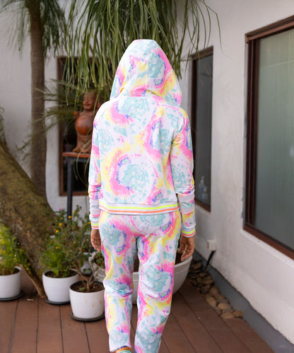 Person in Multicolour Neon Jacket & Joggers Set stands on a wooden deck facing away, with potted plants nearby. This comfy outfit features soft poly blend fabric for a relaxed vibe.