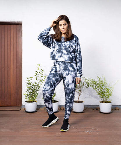 Woman in a Grey and White Sweatshirt-Joggers Set with an oversized cropped sweatshirt, standing on a wooden deck with potted plants behind her.