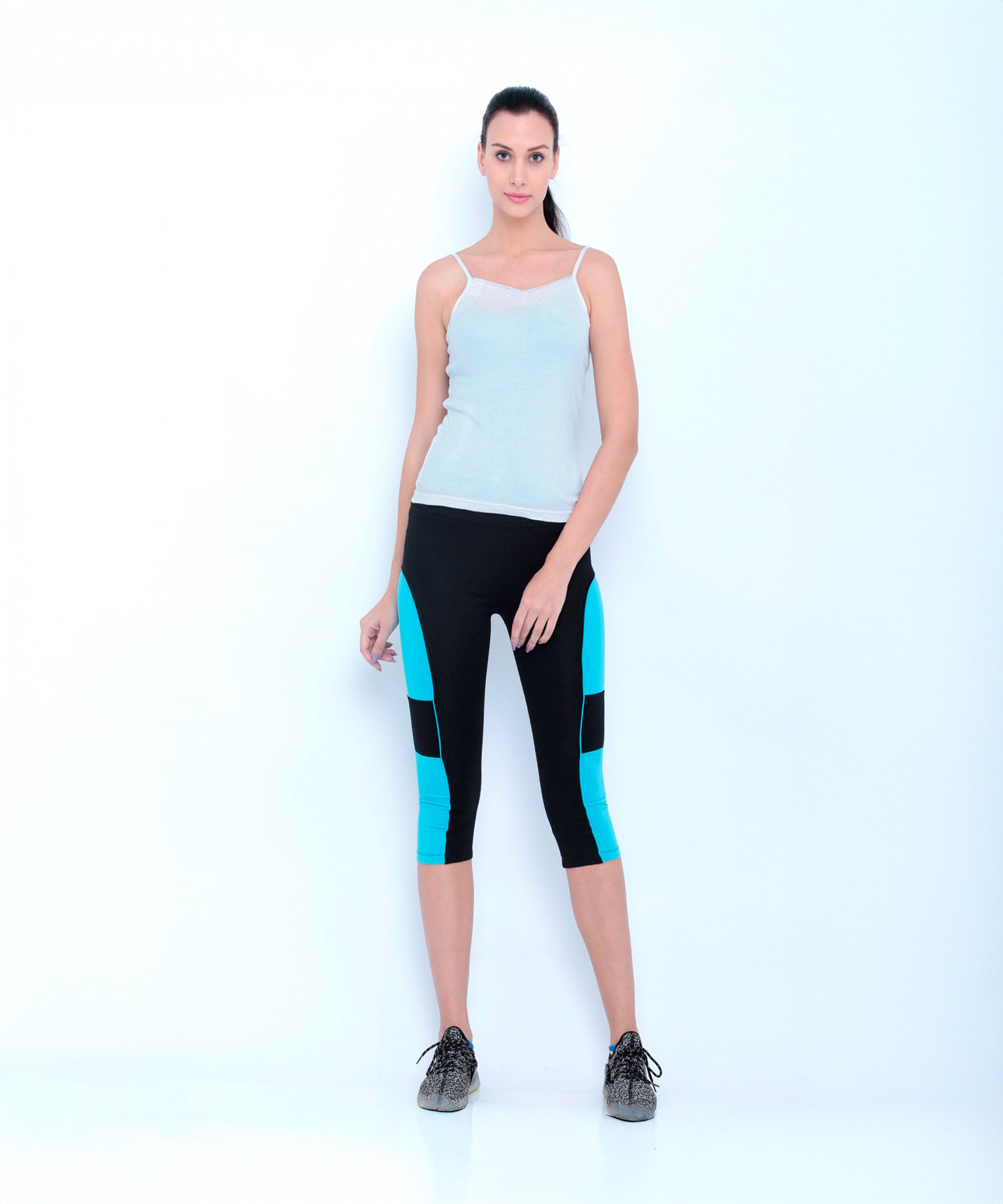 Woman wearing Capri TLC66 black cotton spandex workout pants with blue panels and a white tank top, standing against a plain white background.