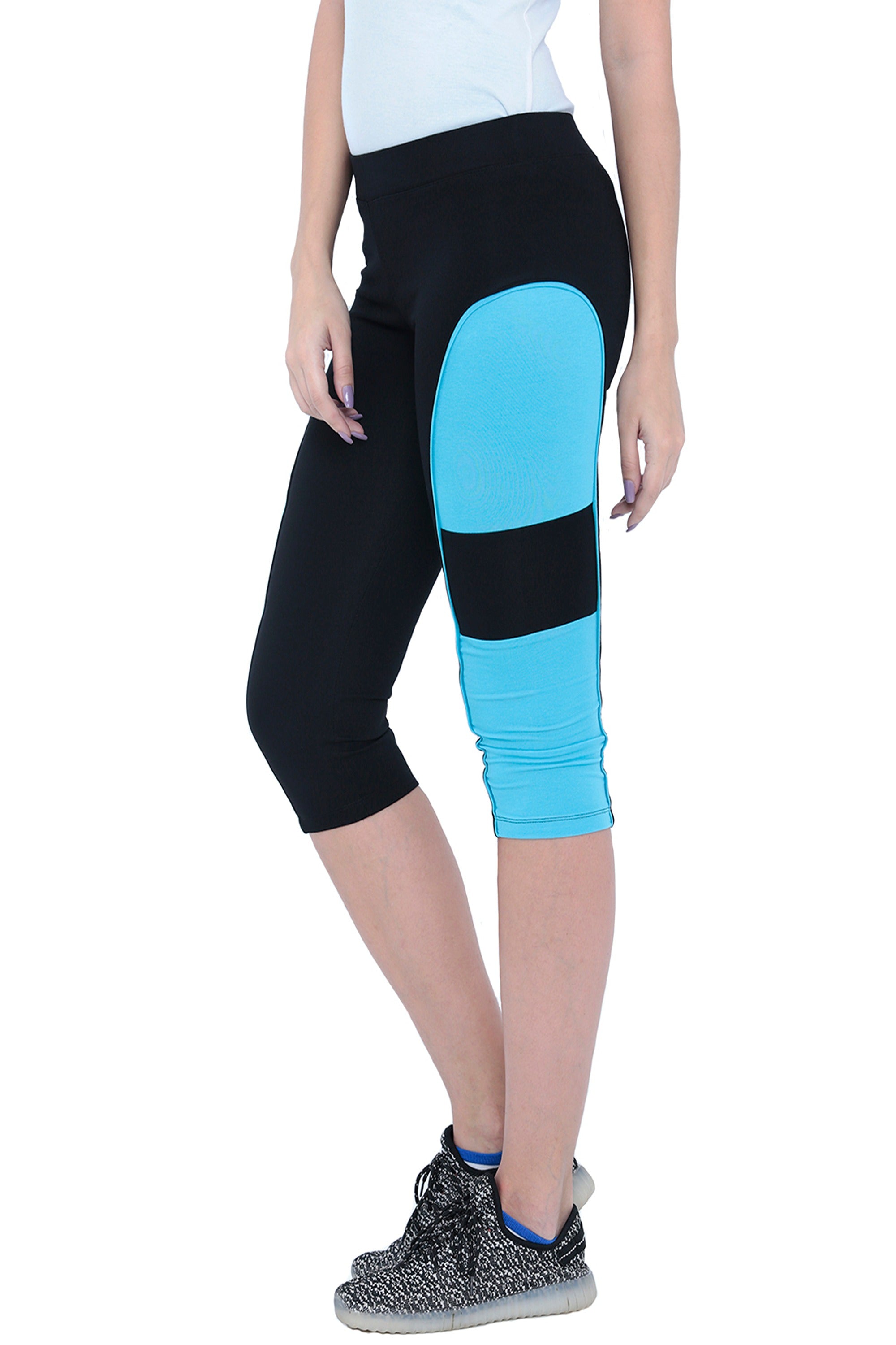A person wearing the Capri TLC66—black capri-length track pants with a blue side panel, made from Cotton Spandex Fabrics for everyday workouts—paired with black sneakers.