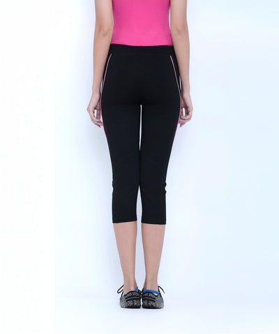 Woman stands with her back to the camera, wearing a pink top and Classic Capri TLC67 leggings with black shoes, highlighting stylish fitness wear.