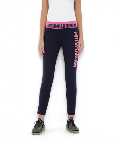 Woman in Classic Capri TLC67 fitness wear—navy capri leggings with a pink waistband, "#TUNALONDON" and "#FITGENERATION" text, paired with sneakers.