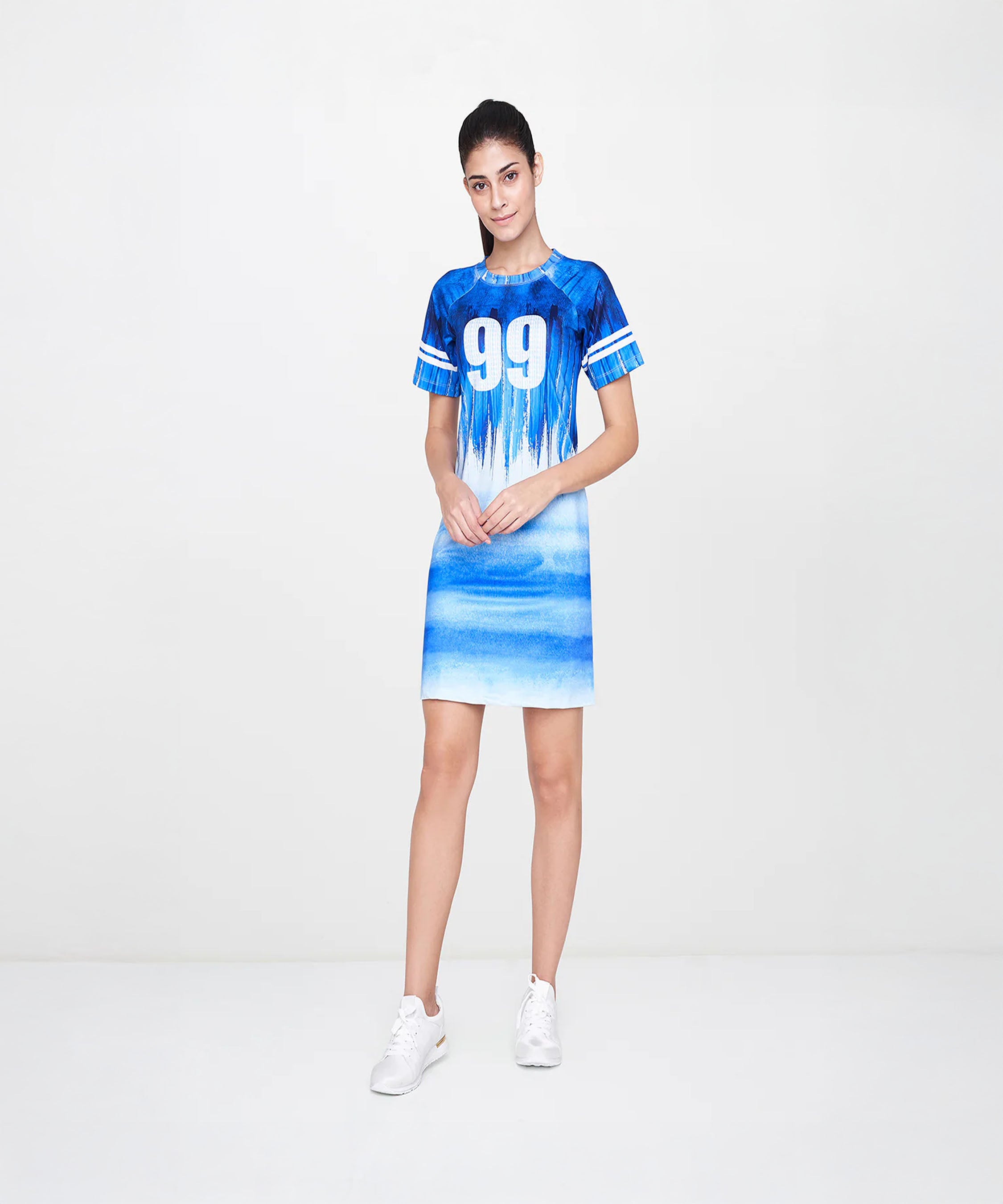A woman wears the Half Sleeve Blue Round Neck Dress—a blue and white sporty dress with number 99, elbow sleeves, and a round neckline—posing against a plain white background.