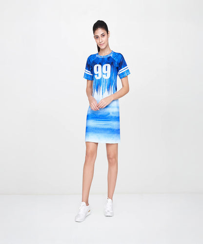 A woman wears the Half Sleeve Blue Round Neck Dress—a blue and white sporty dress with number 99, elbow sleeves, and a round neckline—posing against a plain white background.