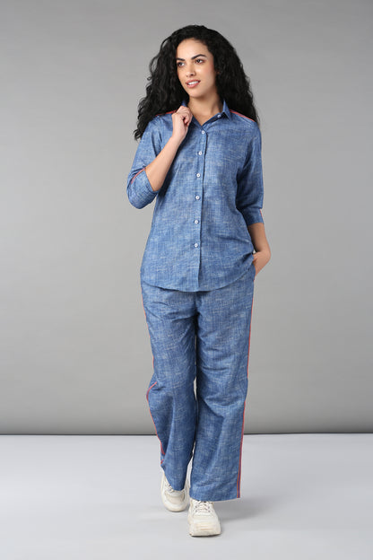 Woman in the Denim Linen Co-Ord Set, featuring a relaxed fit blue button-up shirt and matching pants with red stripes, poses against a plain gray background.