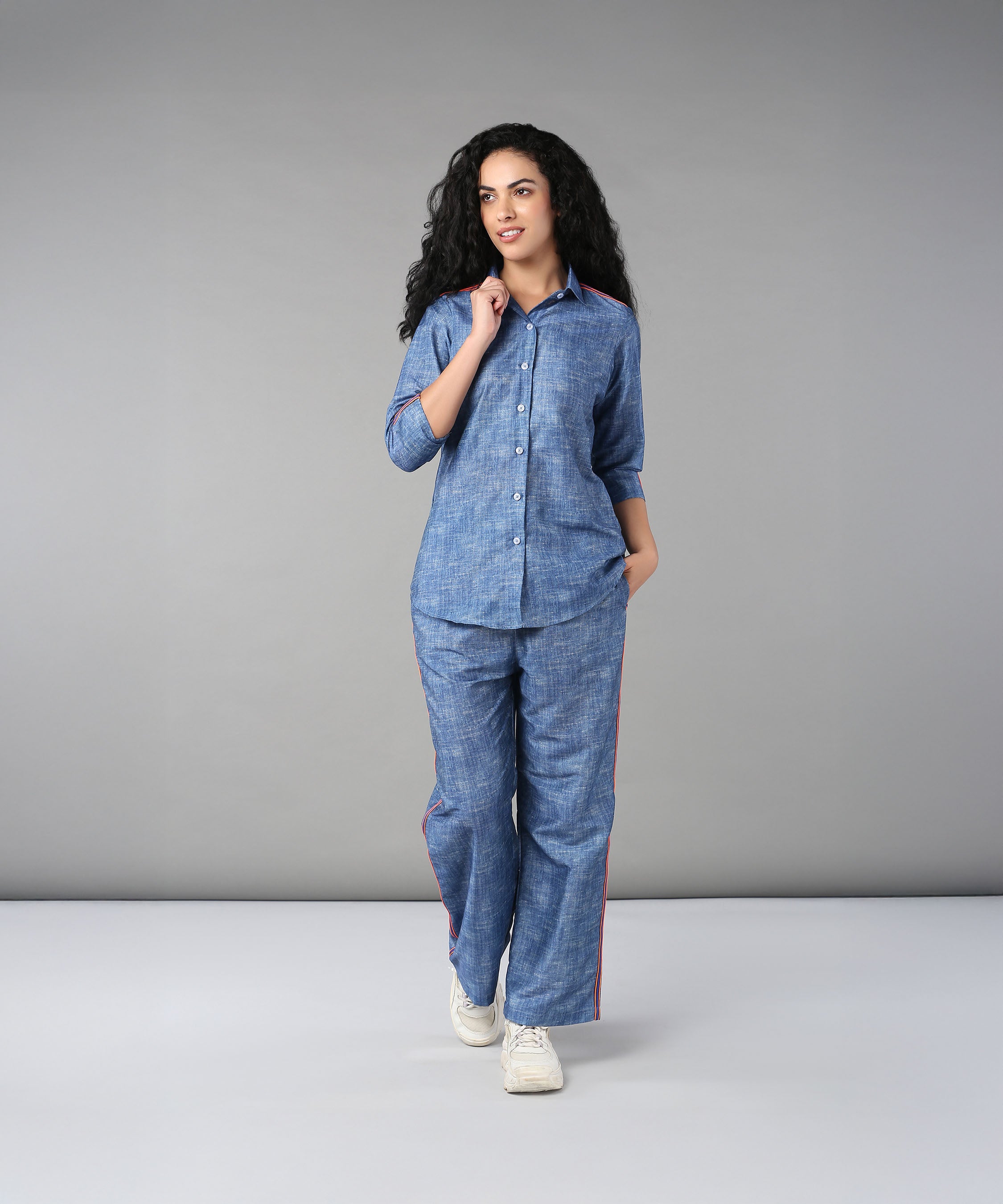 A woman with curly hair walks in a studio wearing the Denim Linen Co-Ord Set, featuring a relaxed fit shirt and matching pants.