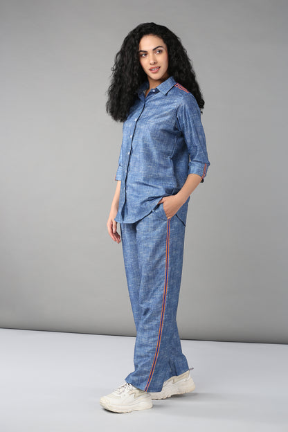 Woman wearing the Denim Linen Co-Ord Set—a high-quality denim ensemble with a full-sleeve relaxed fit shirt and striped pants—paired with white sneakers, standing against a gray background.