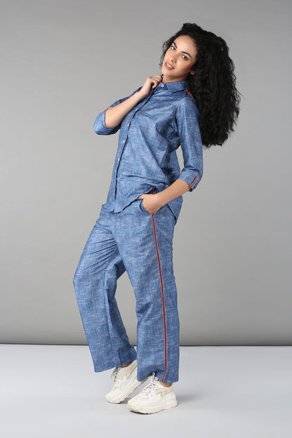 Woman models the Denim Linen Co-Ord Set—a full sleeve, relaxed fit shirt and matching pants with red stripes—styled with white sneakers against a gray backdrop.