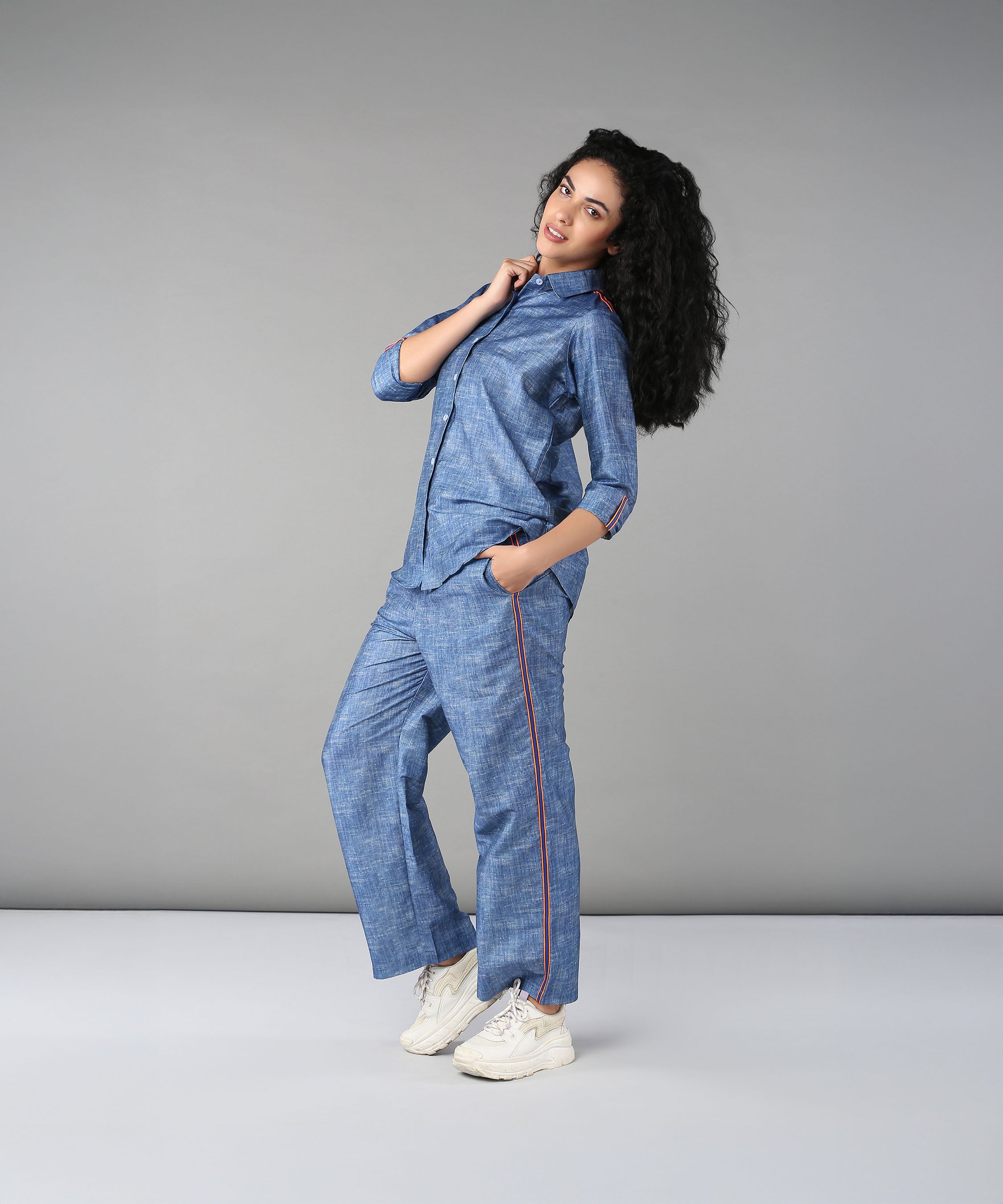 A woman with curly hair models the Denim Linen Co-Ord Set and white sneakers against a plain gray background.