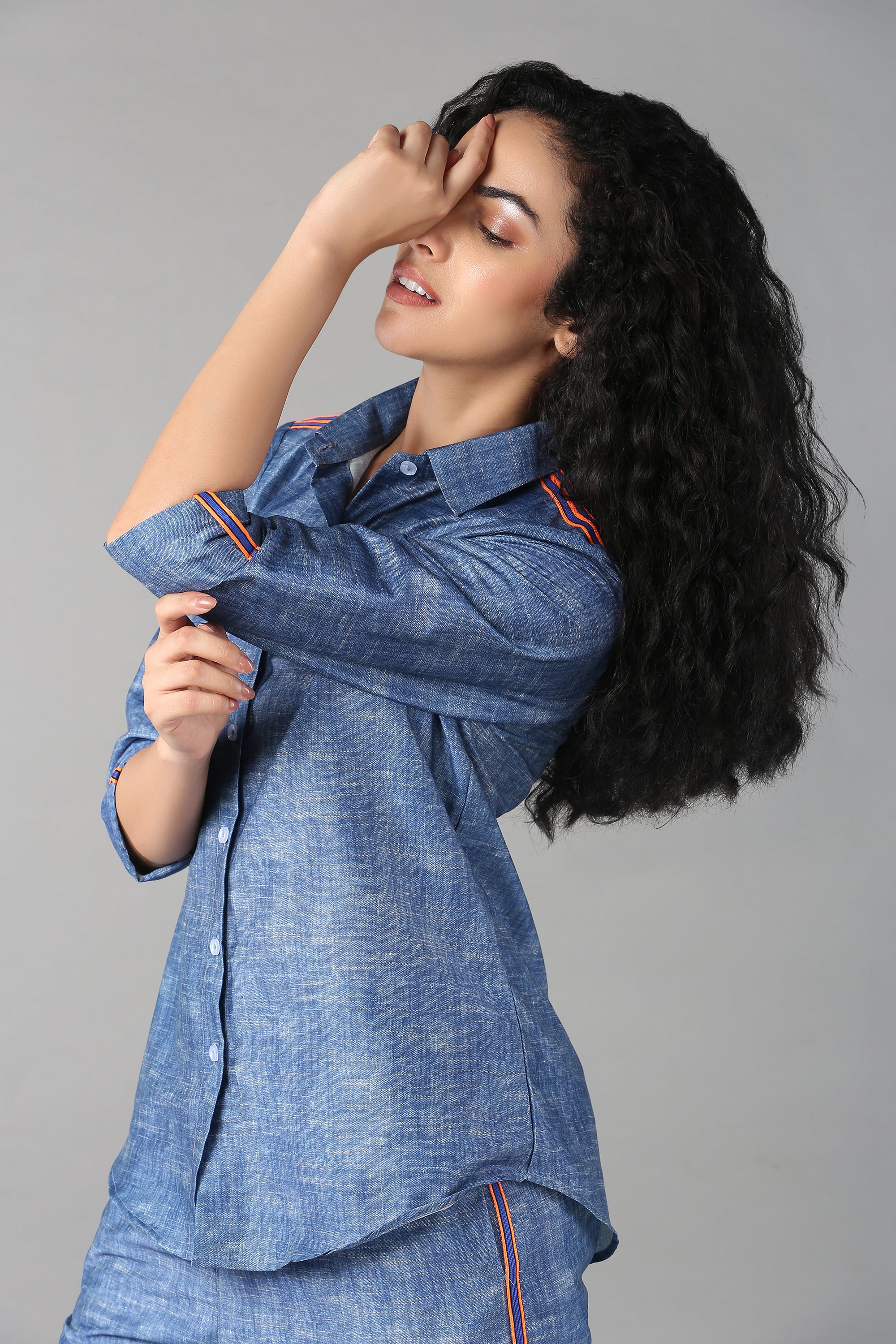 Woman with long curly hair poses with eyes closed, wearing a Denim Linen Co-Ord Set—featuring a full sleeve, relaxed fit shirt.