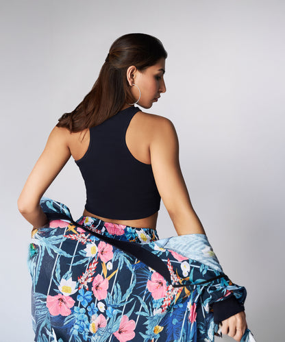A woman with long brown hair, wearing the Tuna Active Floral Co-ord Set—a black sleeveless top and floral skirt—faces away while holding a matching floral bomber jacket.