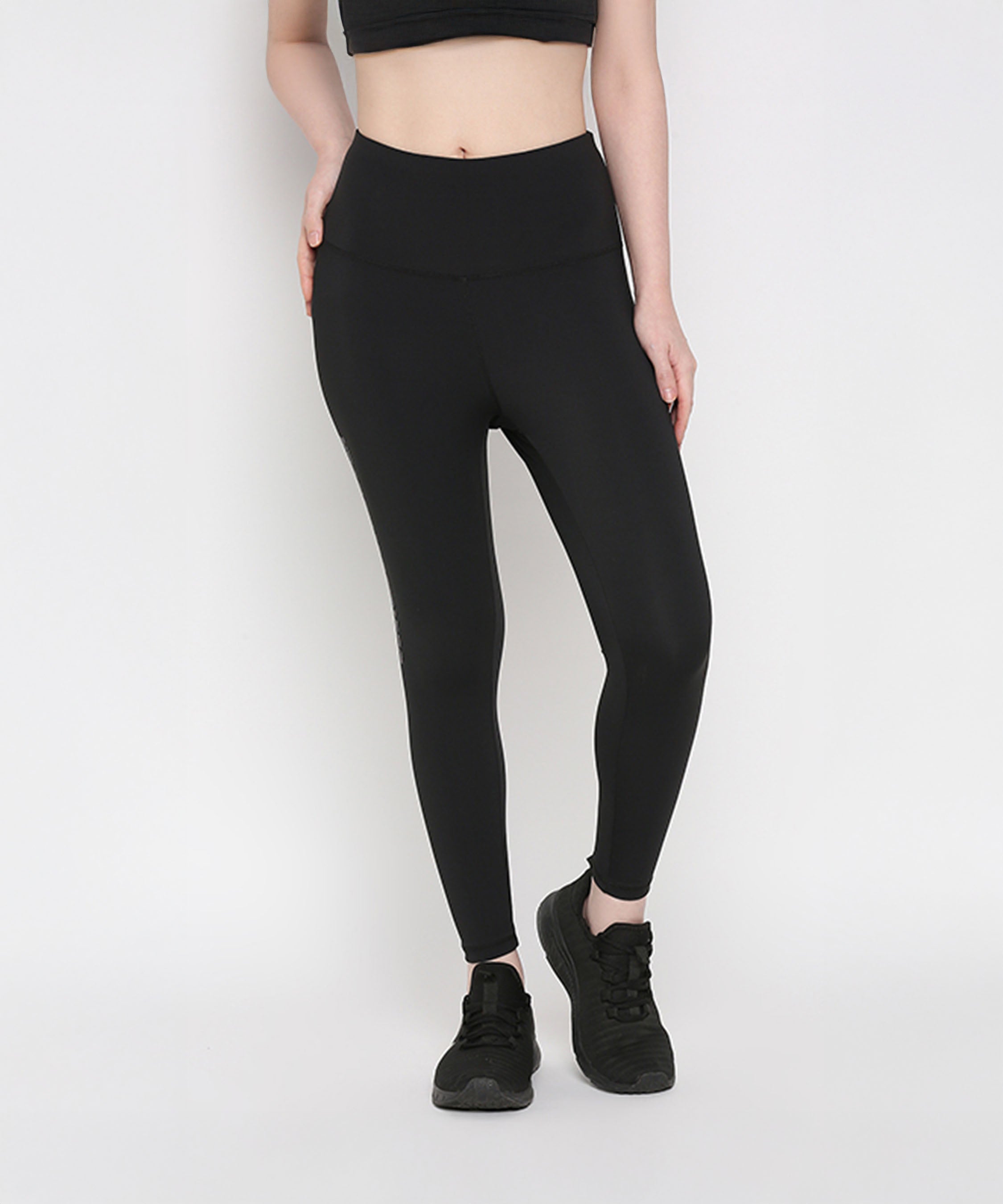 Woman wearing Tuna Active Black Leggings With Print and a black crop top with black sports shoes, standing against a plain white background—ideal for women’s gym wear or yoga leggings enthusiasts.