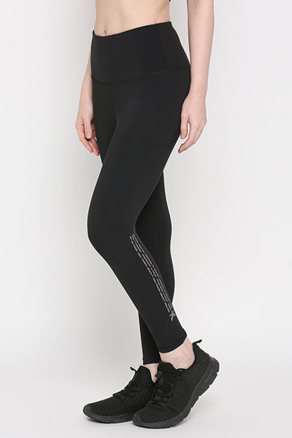 Woman wearing Tuna Active Black Leggings With Print, made from superior stretchable fabric and paired with black sneakers, stands against a plain light background—ideal for yoga, gym, or fitness activities.