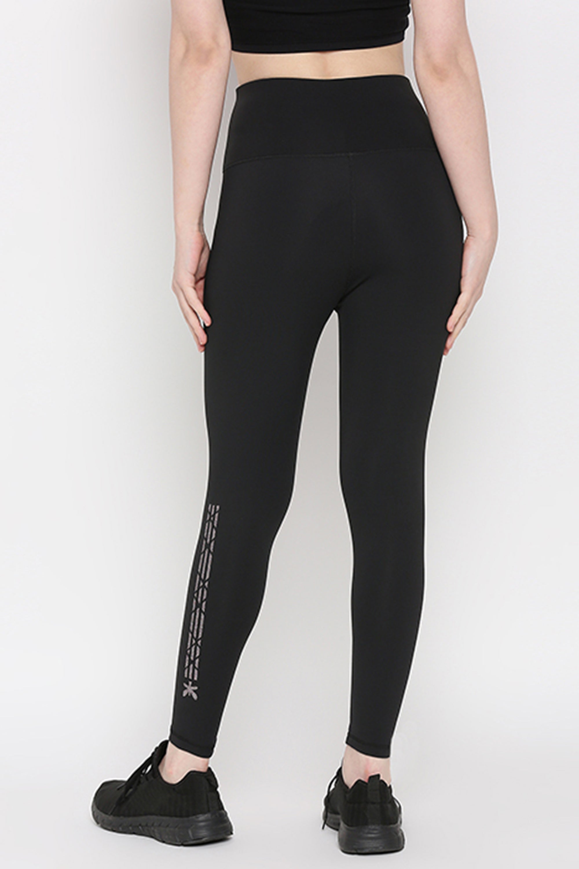 Model wearing Tuna Active Black Leggings With Print and black sneakers, shown from the back on a plain white background. Made of superior quality stretchable fabric, ideal for yoga, gym, sports, or fitness activities.