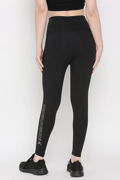 Model wearing Tuna Active Black Leggings With Print and black sneakers, shown from the back on a plain white background. Made of superior quality stretchable fabric, ideal for yoga, gym, sports, or fitness activities.