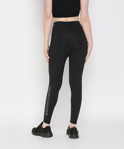Person in Tuna Active Black Leggings With Print, facing away from the camera; stretchy workout pants feature a design on the lower leg.