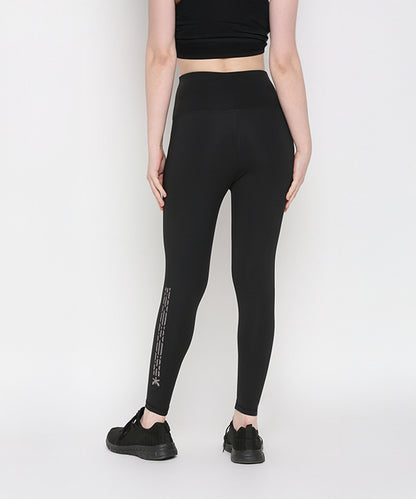 Person in Tuna Active Black Leggings With Print, facing away from the camera; stretchy workout pants feature a design on the lower leg.
