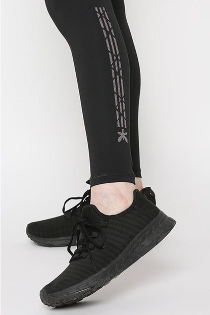 Person wearing Tuna Active Black Leggings With Print and black athletic shoes, standing on a white background—ideal for yoga, gym, sport, and fitness activities.