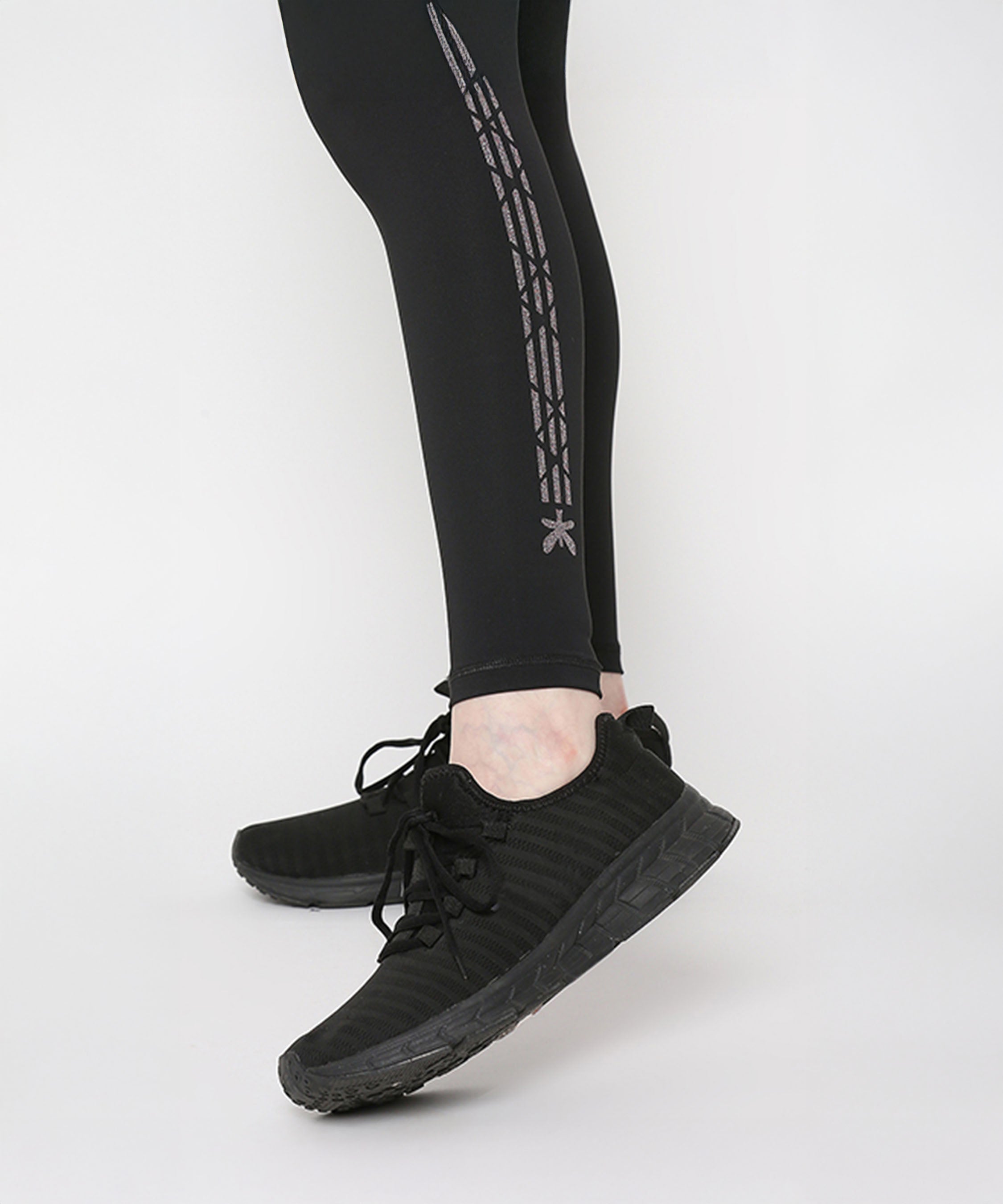 Person wearing Tuna Active Black Leggings With Print and black athletic shoes, standing on a white floor.