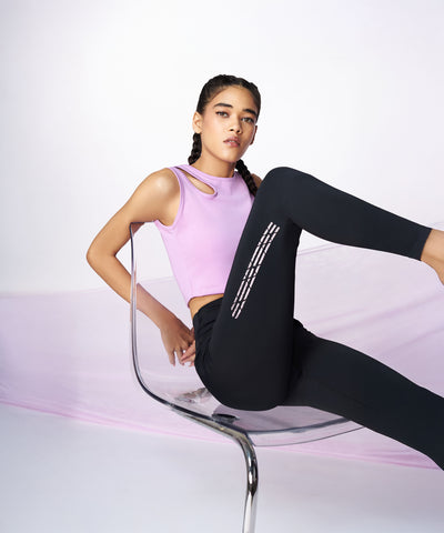 Woman sitting confidently on a clear chair, wearing a sleeveless pink top and Tuna Active Black Leggings With Print—stylish, stretchable workout pants perfect for women’s gym wear.