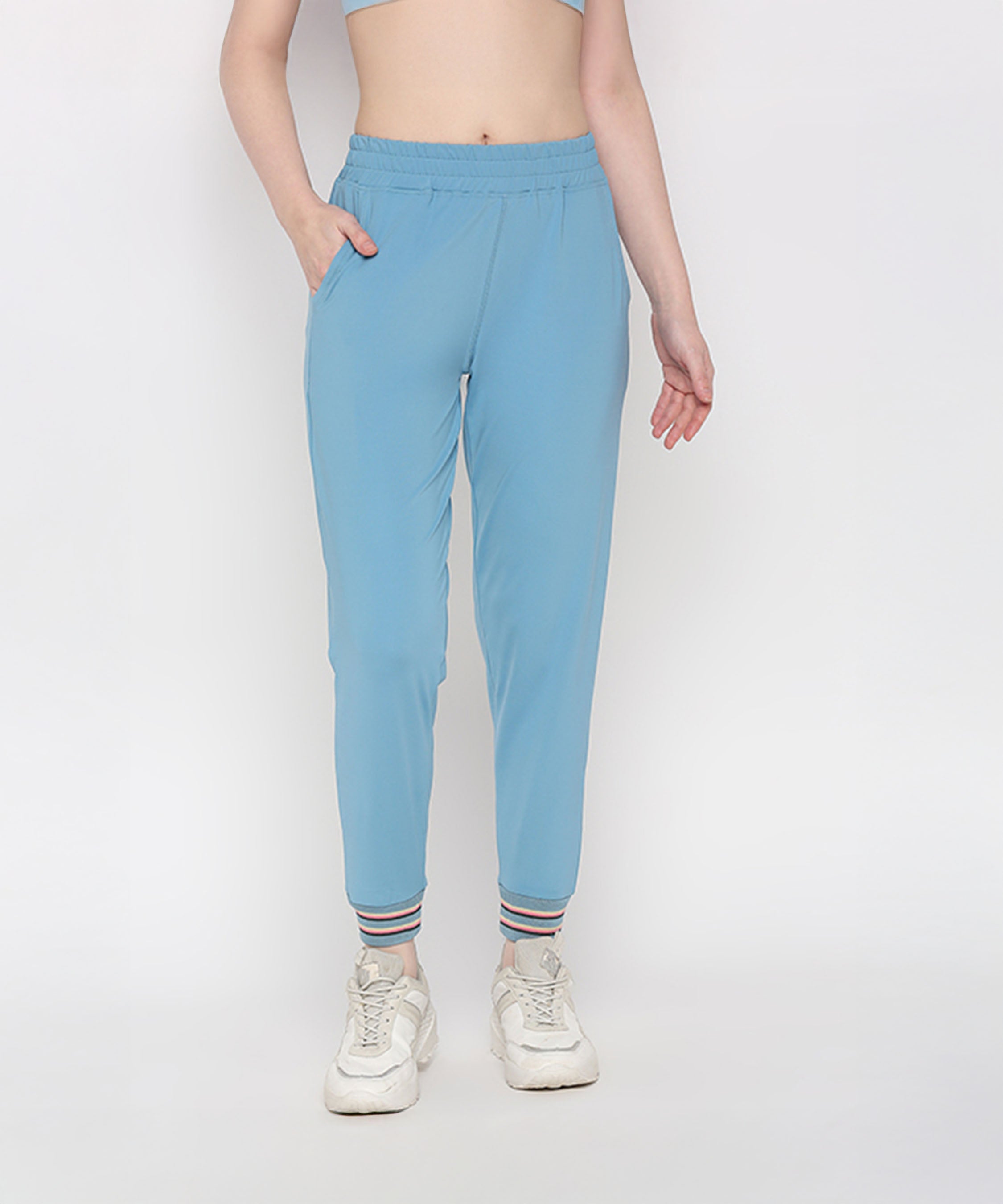 A woman stands against a plain white background wearing Tuna Active Blue Joggers paired with white sneakers.