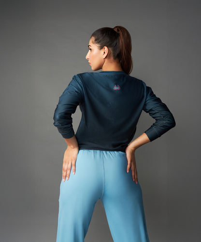 A woman faces away in a dark top and Tuna Active Blue Joggers, standing against a plain gray background.