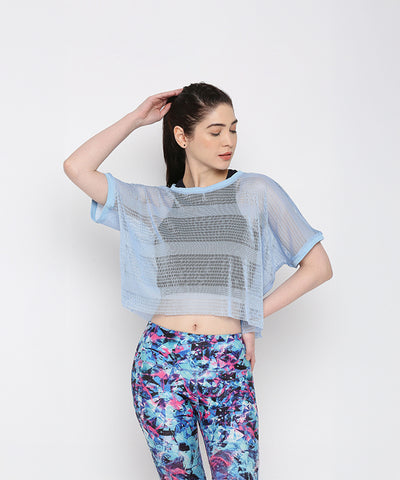 A woman models the Blue Netted Top layered over a black sports bra and vibrant floral leggings, posing against a plain background for a chic, sporty vibe.