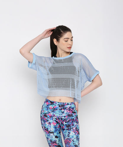 A woman models the Blue Netted Top layered over a black sports bra and vibrant floral leggings, posing against a plain background for a chic, sporty vibe.