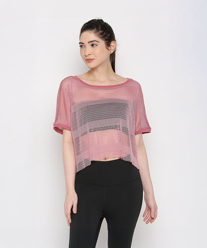 A woman showcases the Pink Netted Top, worn sheer over a black sports bra and paired with stylish leggings, creating a trendy sporty look against a white background.