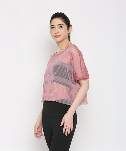 A woman models the Pink Netted Top with chic leggings, standing sideways against a plain white background to highlight her sporty style.