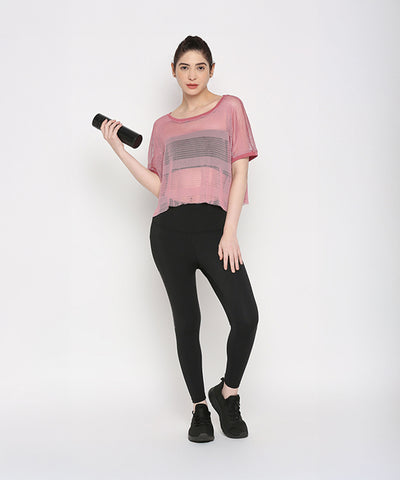 Woman wearing a Pink Netted Top and stylish leggings holds a water bottle, highlighting a sporty look against a plain white background.