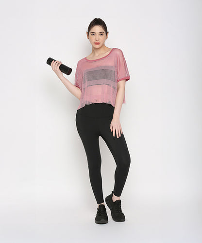 Woman wearing a Pink Netted Top and stylish leggings holds a water bottle, highlighting a sporty look against a plain white background.