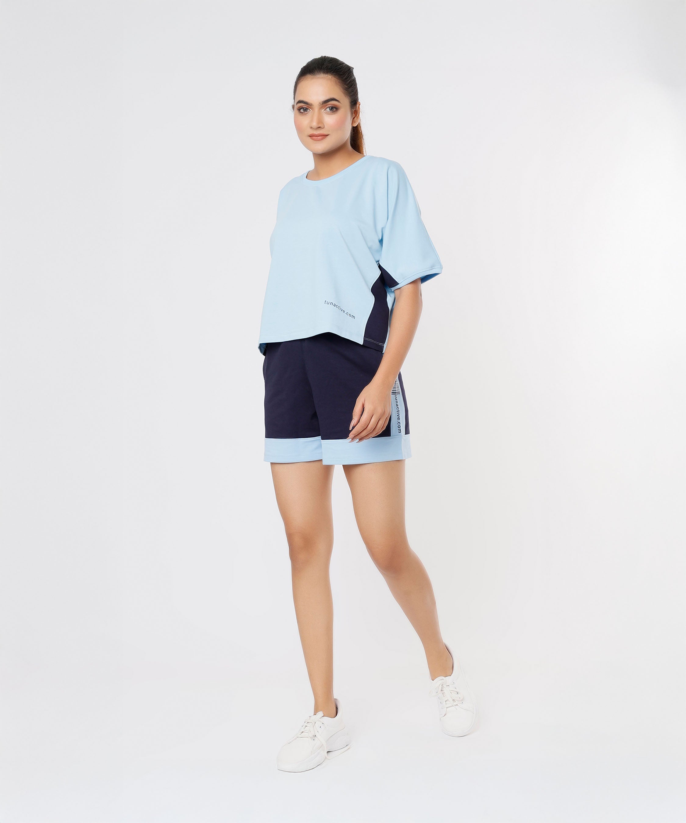 Woman wearing the Tuna Active Blue Tee and navy shorts made from soft Cotton Lycra with sneakers, standing against a plain white background.