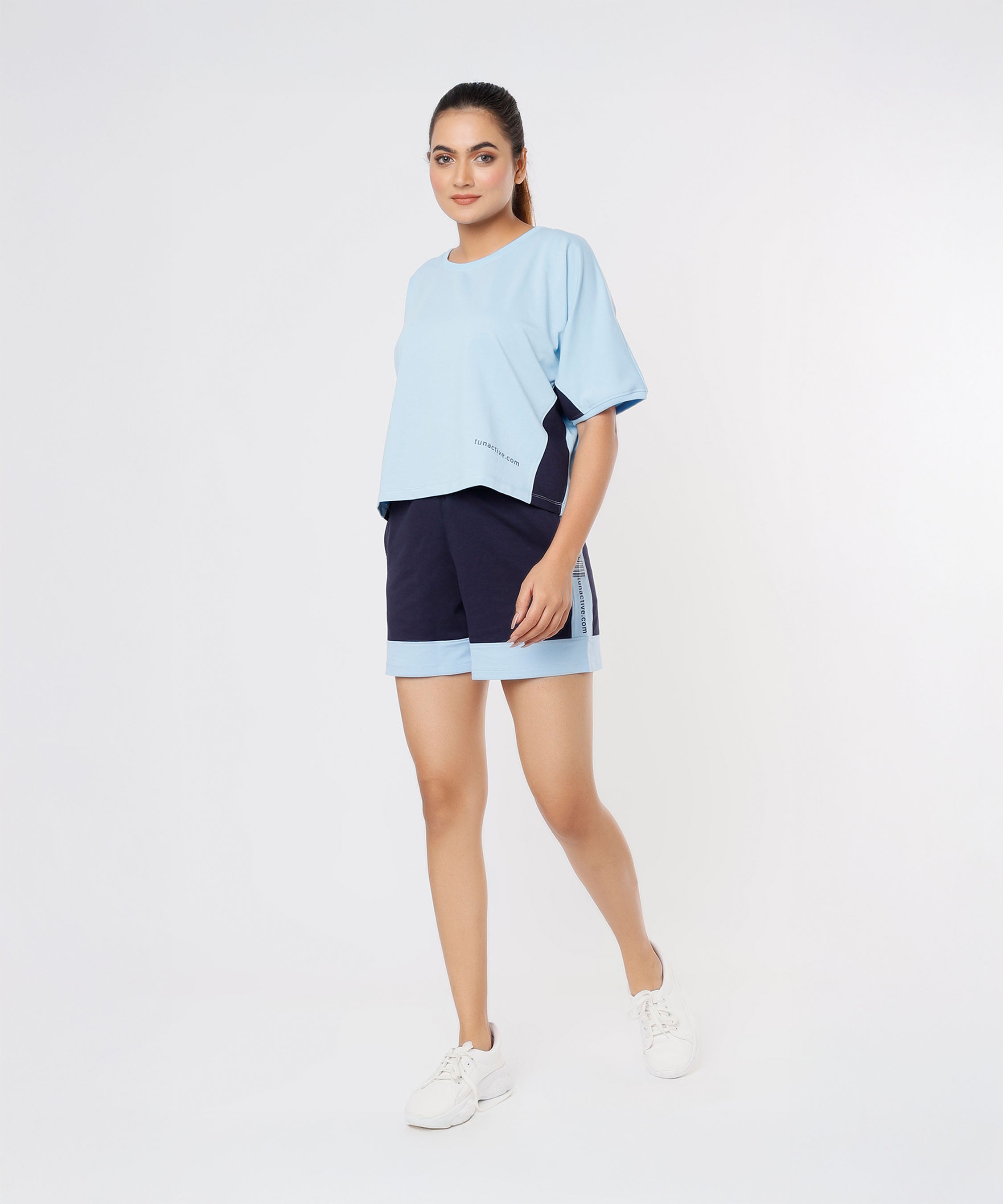 A woman walks against a white background wearing Tuna Active Barcode Printed Blue Shorts. These shorts offer comfort and style, making them perfect for a casual co-ord set.